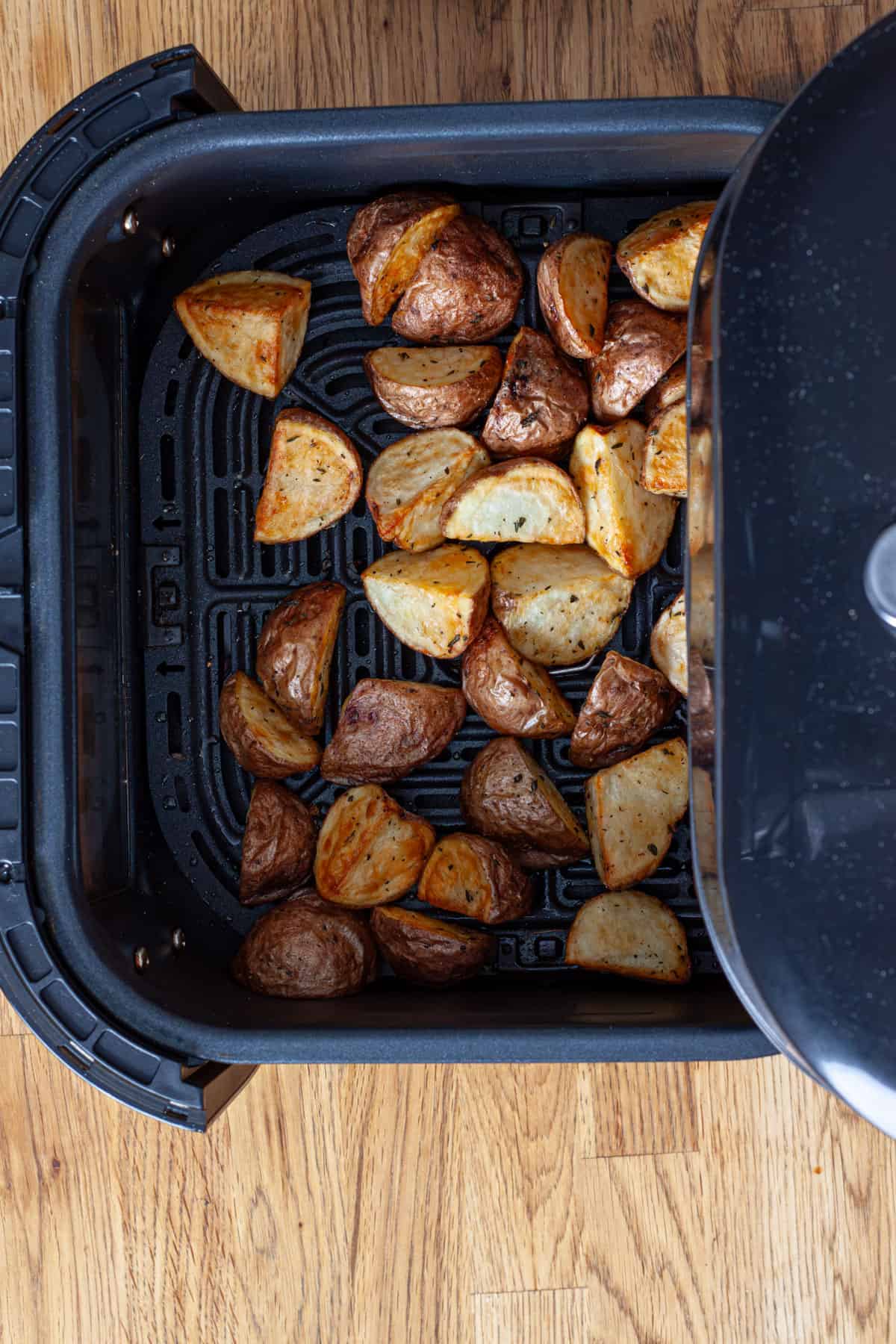 An air fryer basket with crispy seasoned small red potatoes.
