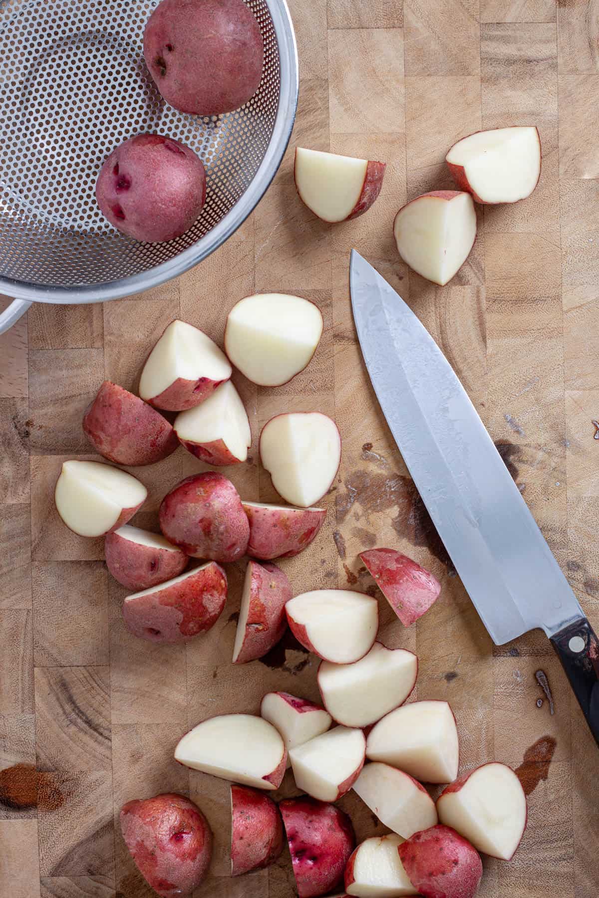Red potatoes on a butcherblock cutting board getting chopped.