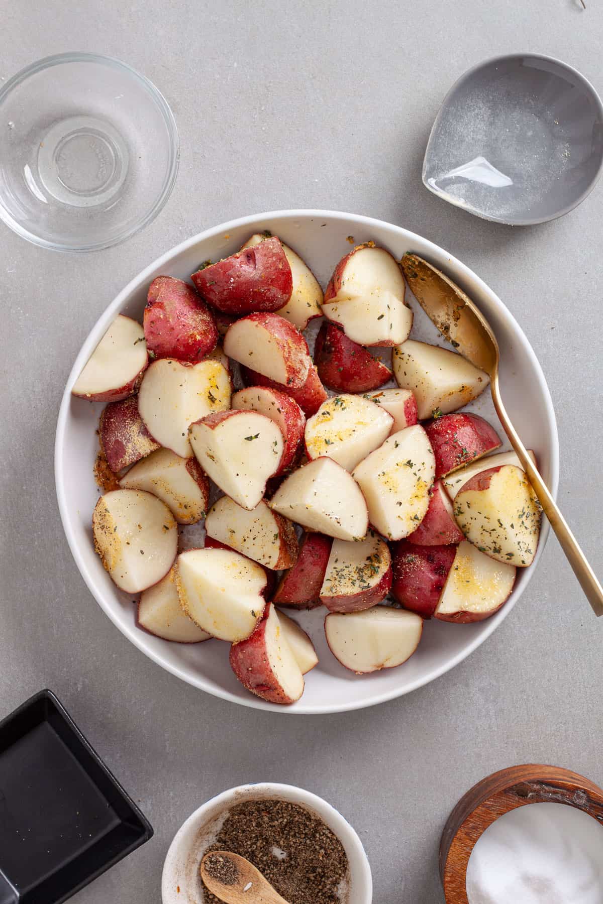 A bowl of chopped red potatoes seasoned with garlic powder, oil and fresh thyme.