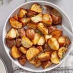 A serving bowl of crispy air fried red potatoes garnished with sprigs of fresh thyme.