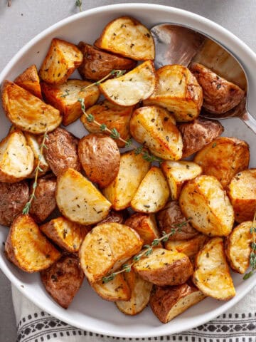 A serving bowl of crispy air fried red potatoes garnished with sprigs of fresh thyme.