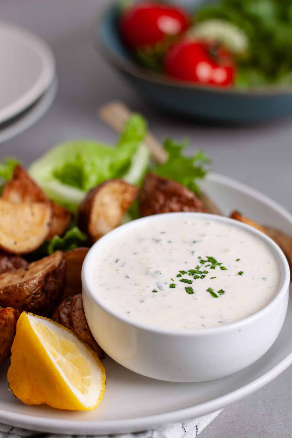 A small bowl with horseradish aioli topped with fresh chives on a plate with crispy fried potatoes.