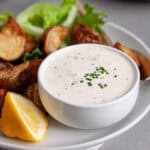 A closeup of horseradish aioli in a small bowl on a platter of crispy roasted potatoes.