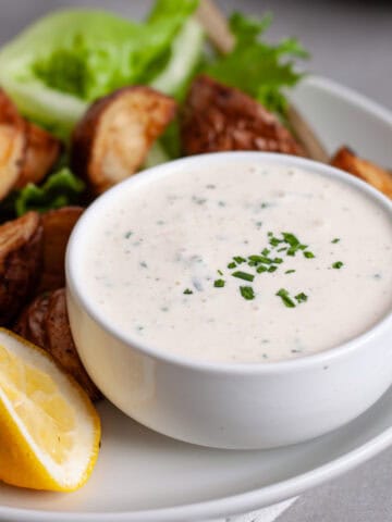 A closeup of horseradish aioli in a small bowl on a platter of crispy roasted potatoes.