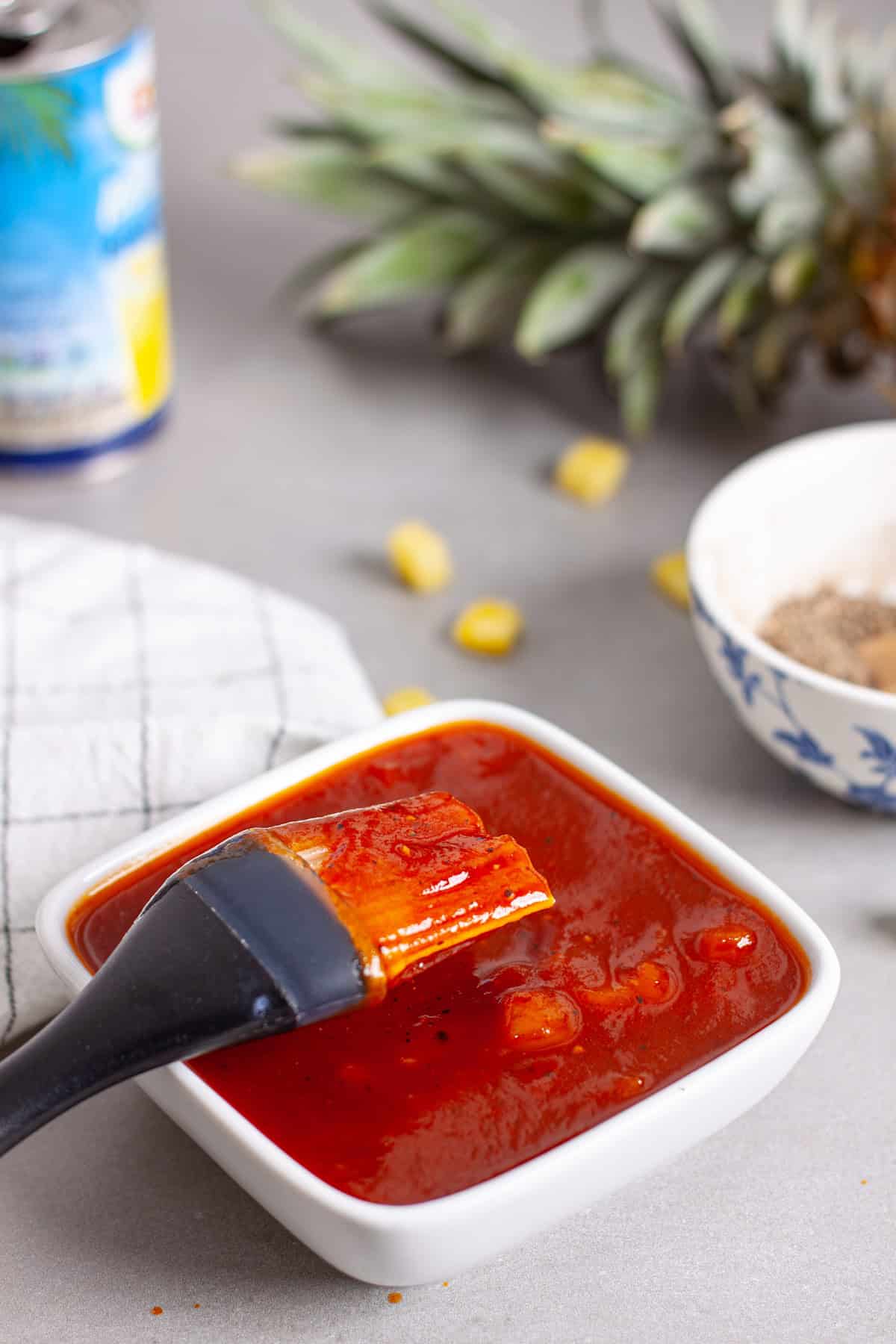 Pineapple bbq sauce in a small bowl with diced pineapple in the background.