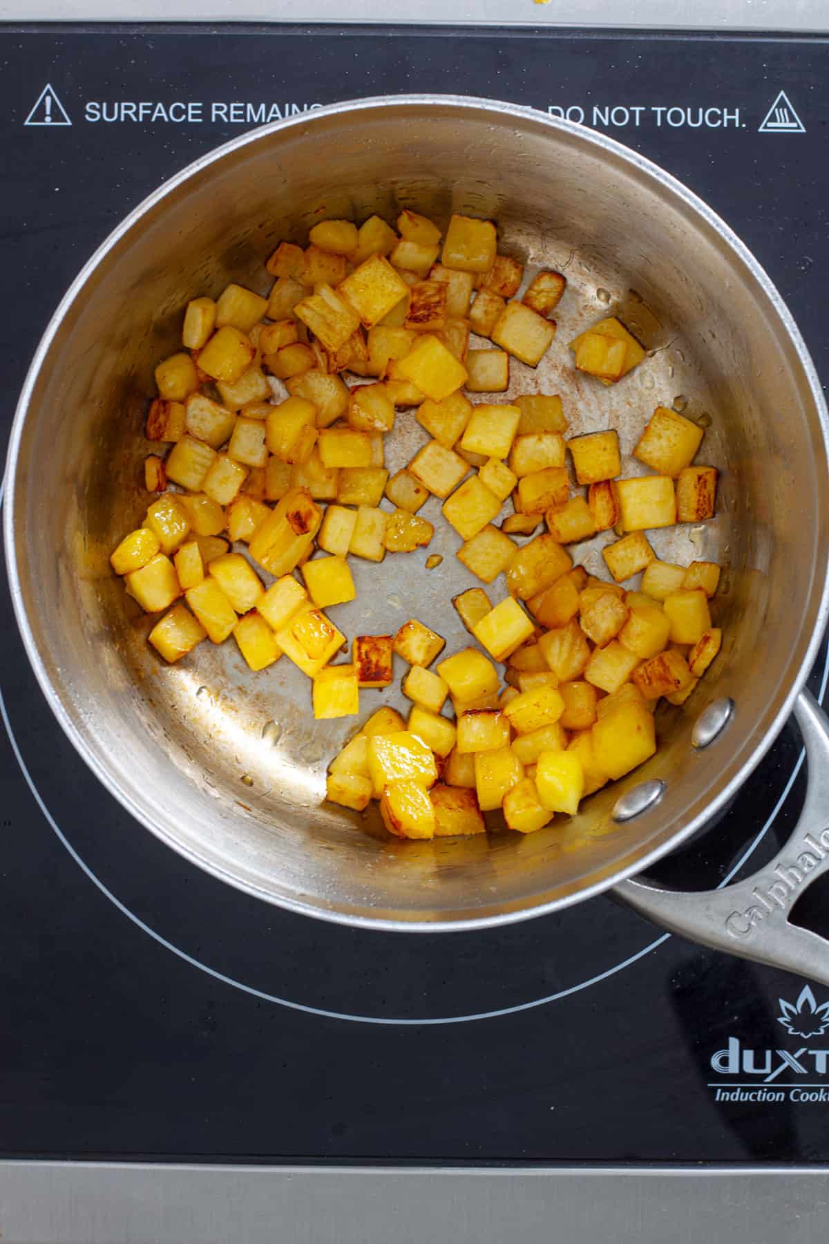 Diced pineapple in a small saucepan getting charred to golden brown.