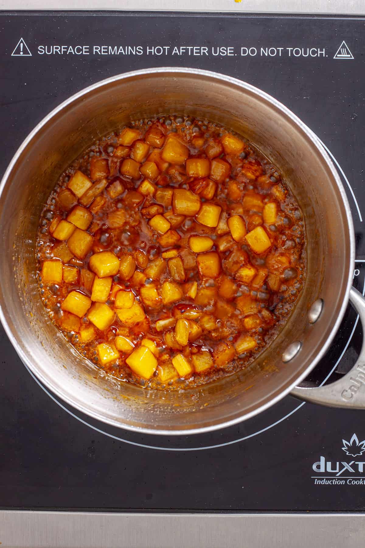 Brown sugar and charred pineapple simmering in a small saucepan.