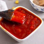 A small bowl of pineapple bbq sauce with a brush inside and a chopped pineapple in the background.