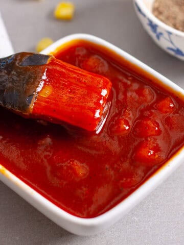 A small bowl of pineapple bbq sauce with a brush inside and a chopped pineapple in the background.
