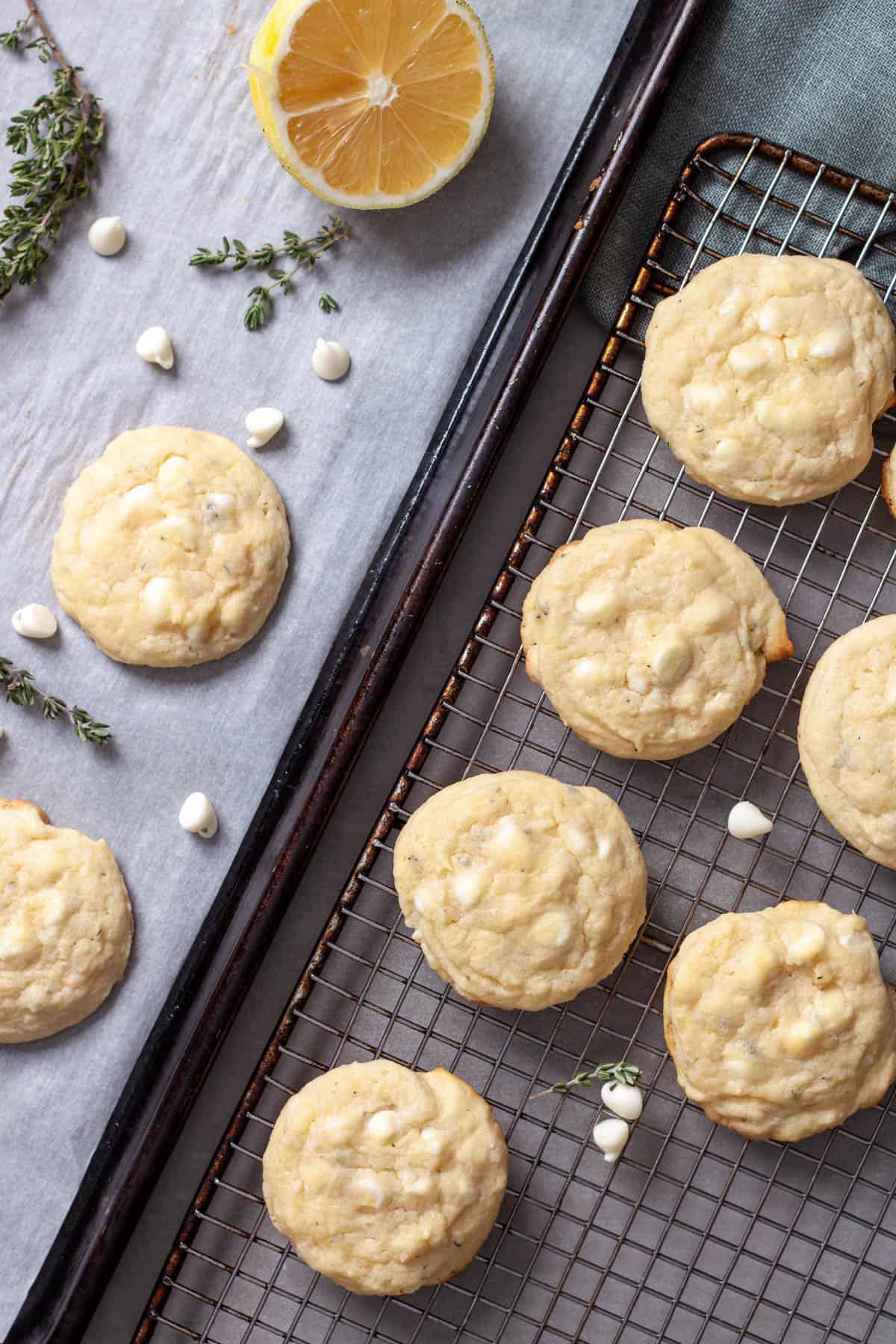 White chocolate and lemon cookies cooling on a wire rack with fresh thyme and white chocolate chips scattered.