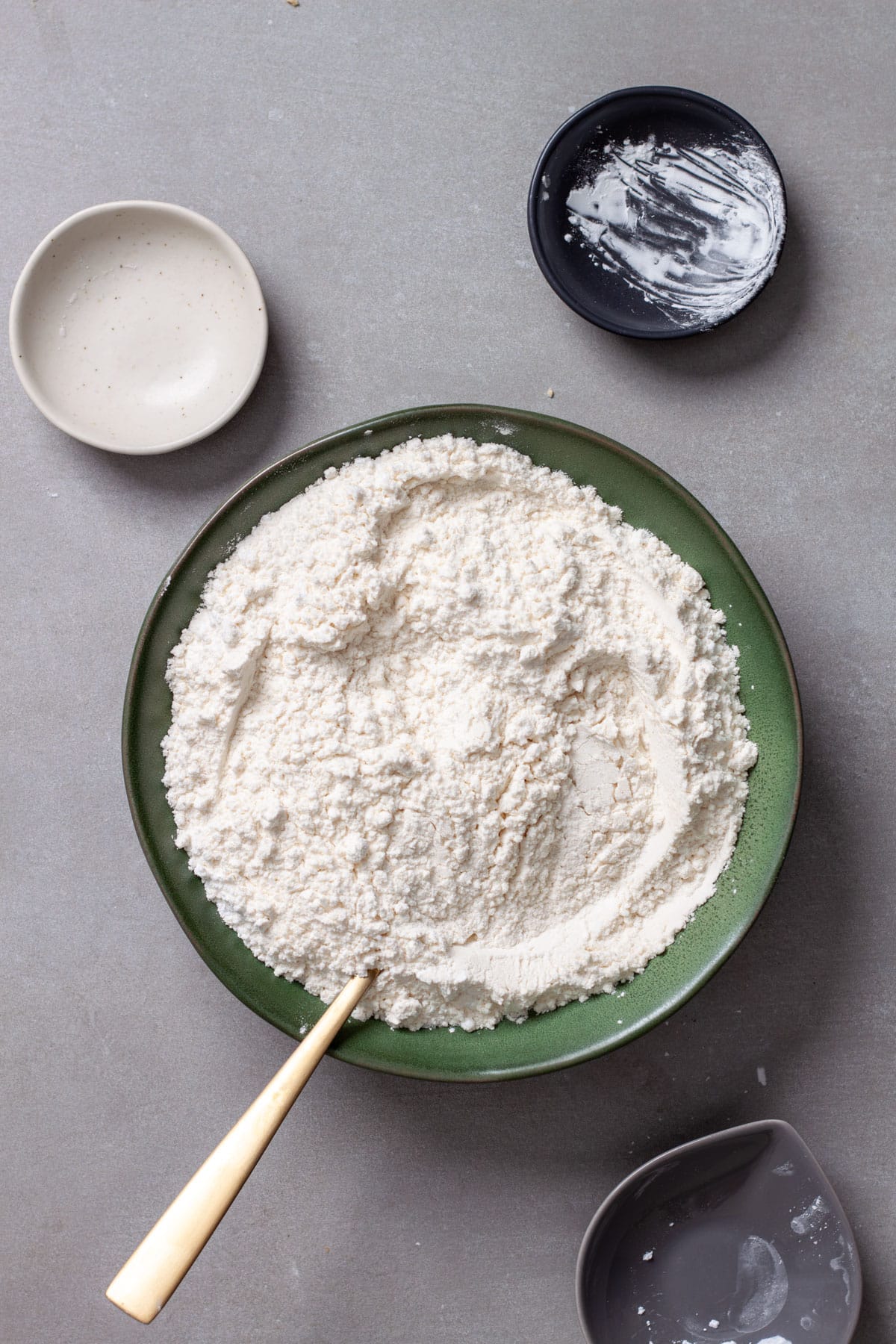 Dry ingredients for lemon white chocolate cookies in a green bowl getting stirred by a whisk.