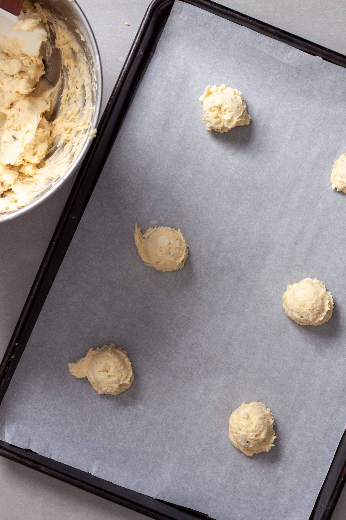 A parchment paper lined baking sheet with lemon white chocolate chip cookie dough scooped into small balls on top.
