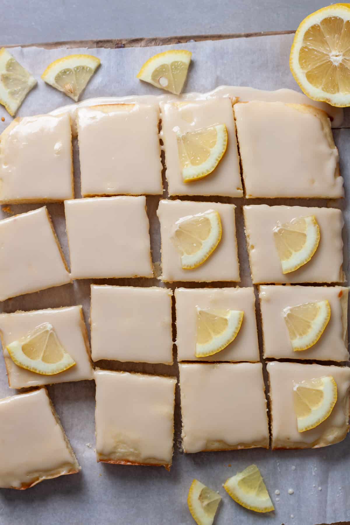 Thin slices of lemons pressed on top of lemon blondies on a piece of parchment paper.