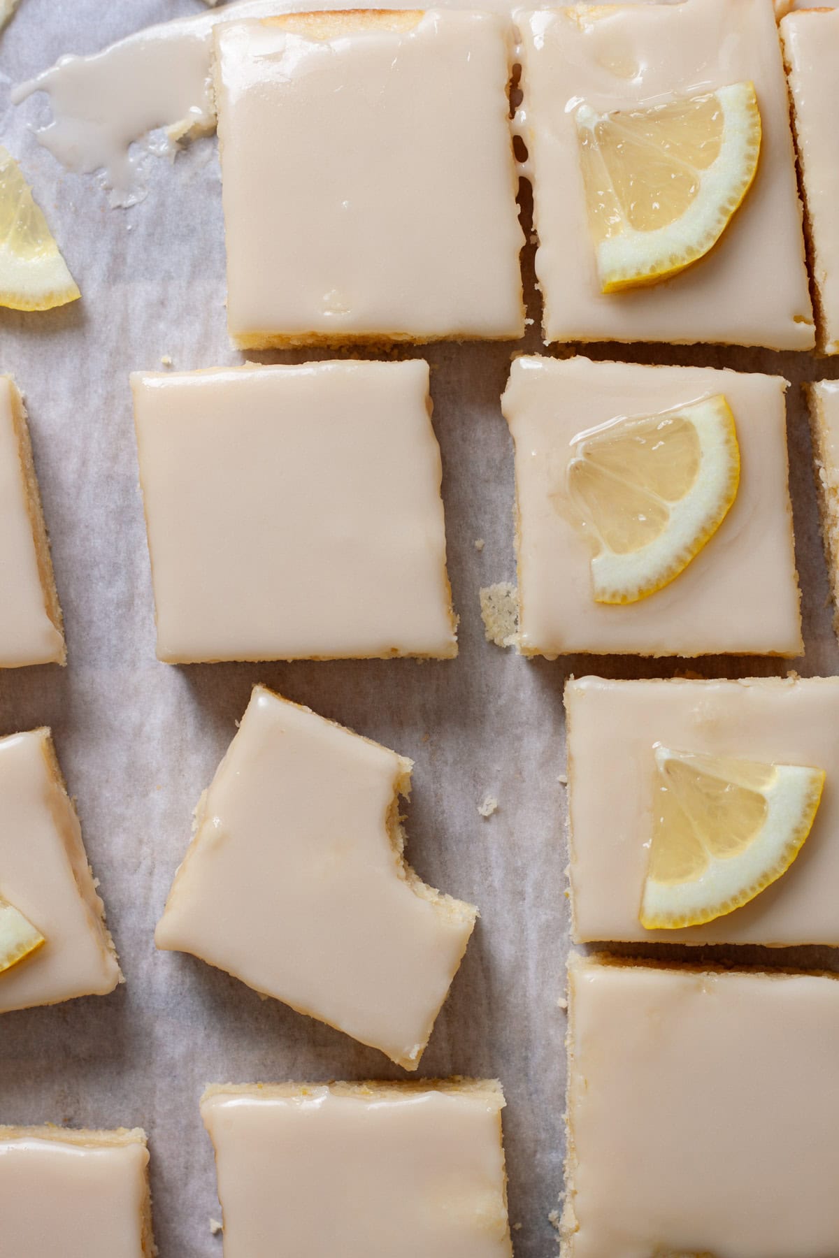 Lemon blondies topped with thin slices of lemon on a piece of parchment paper.