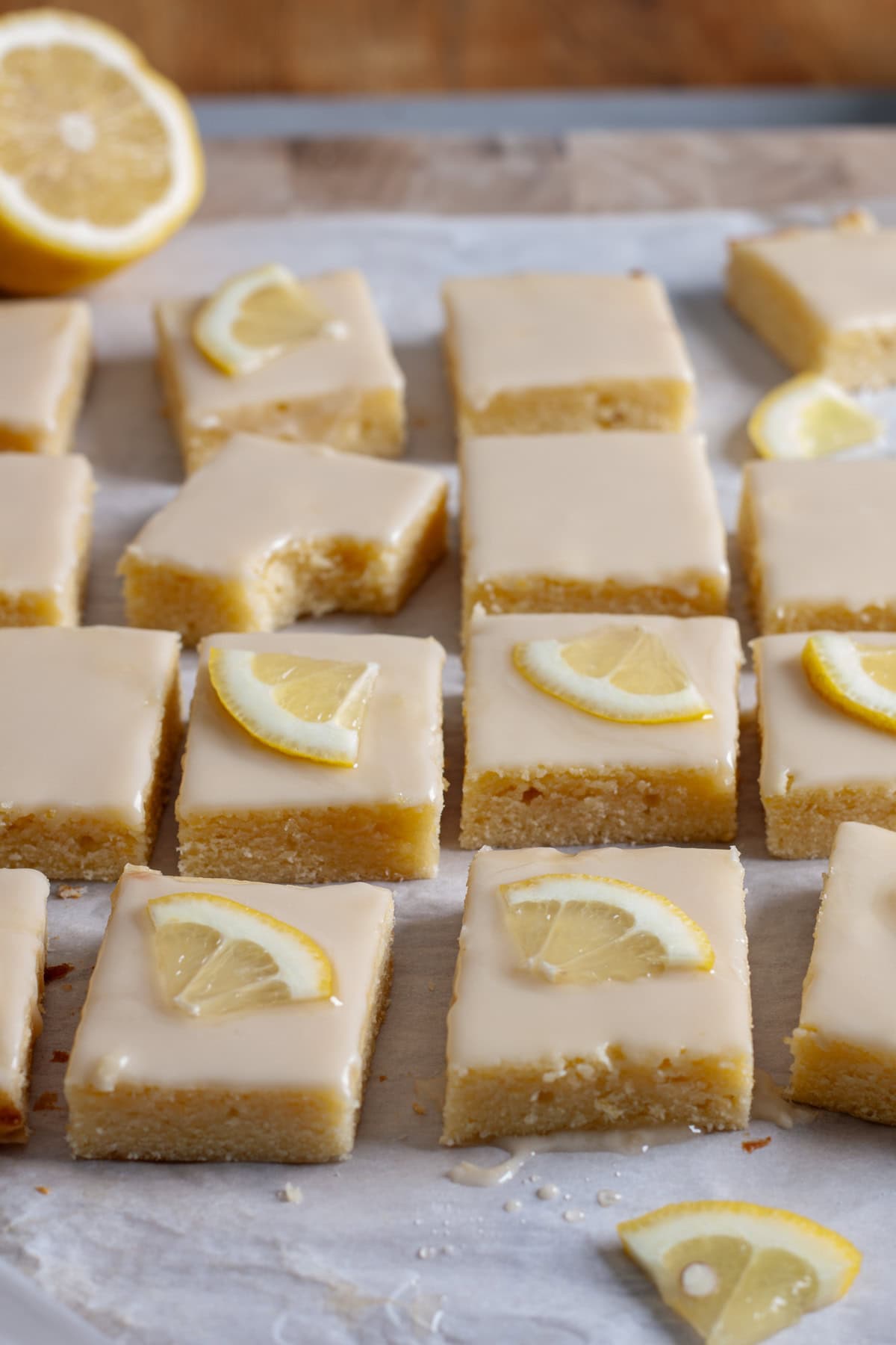 Lemon blondies topped with thin slices of lemon on a piece of parchment paper.