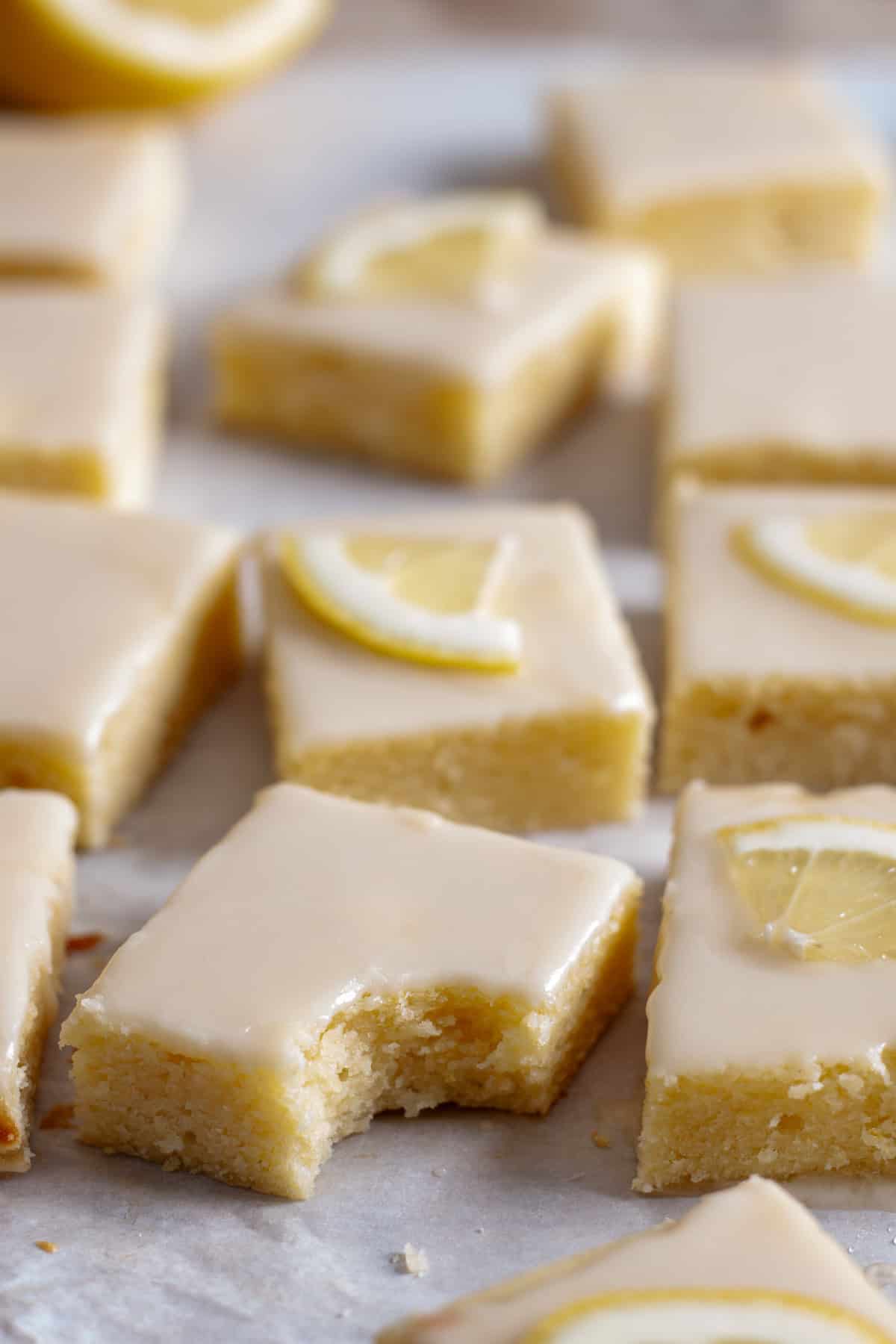 Lemon blondies on parchment paper and one blondie has a bite taken out of it.