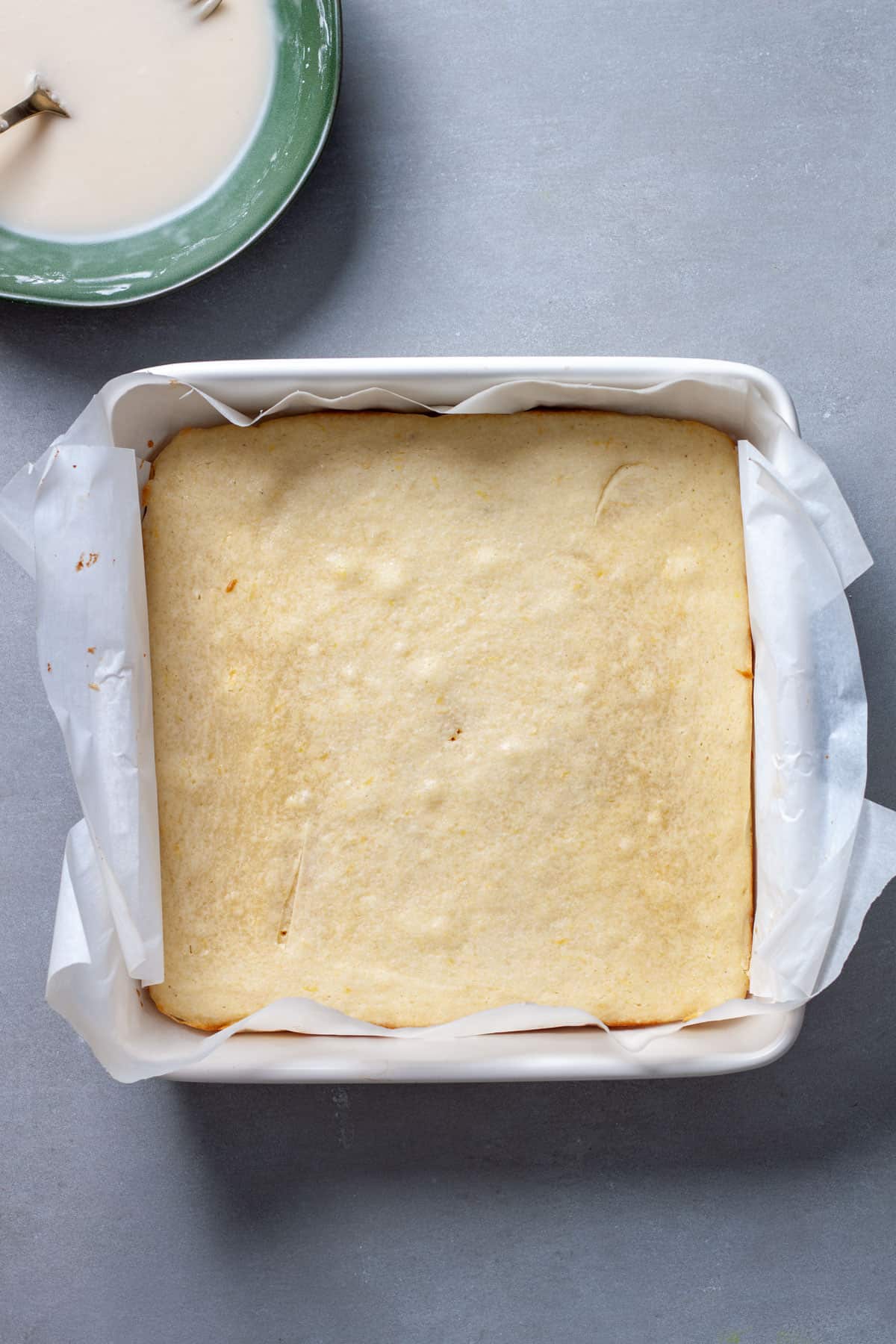 Lemon blondies fresh out of the oven cooling on a gray table with icing off to the side.