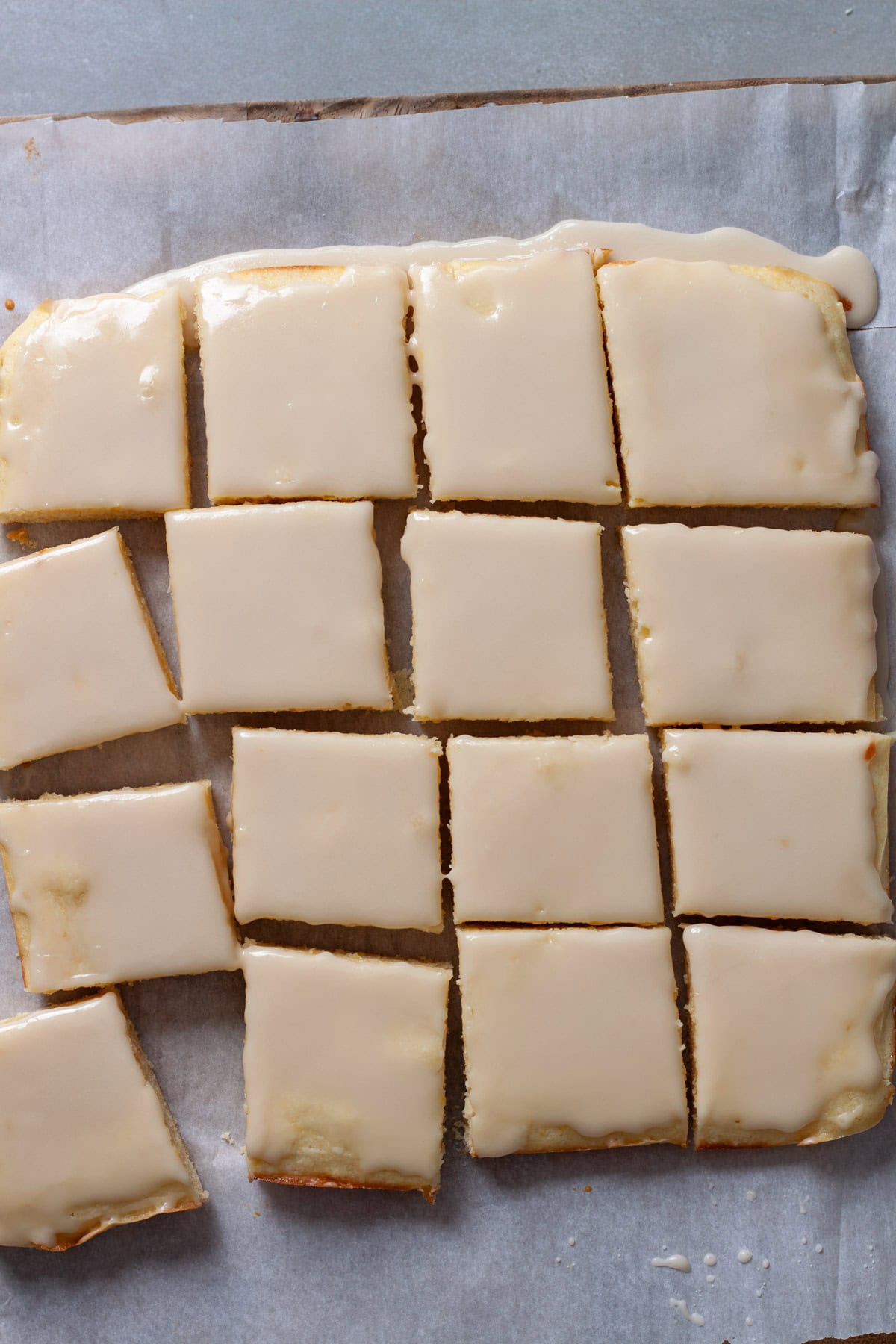 Lemon blondies topped with lemon icing cut up on a piece of parchment paper on a cutting board.