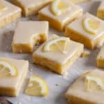 Lemon blondies topped with thin slices of lemon on a piece of parchment paper.