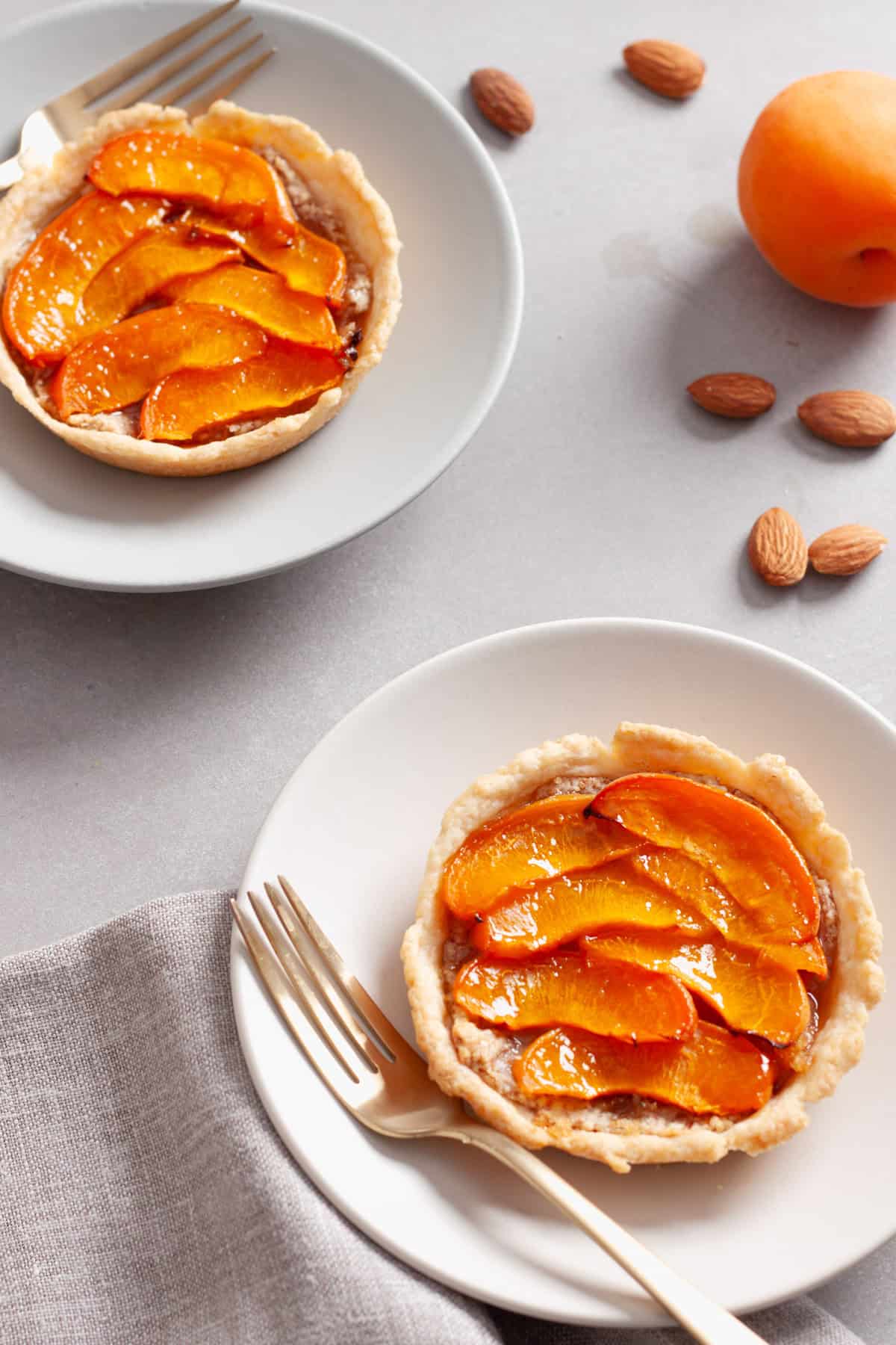 Two servings of apricot tarts with almonds on small plates on a gray table.