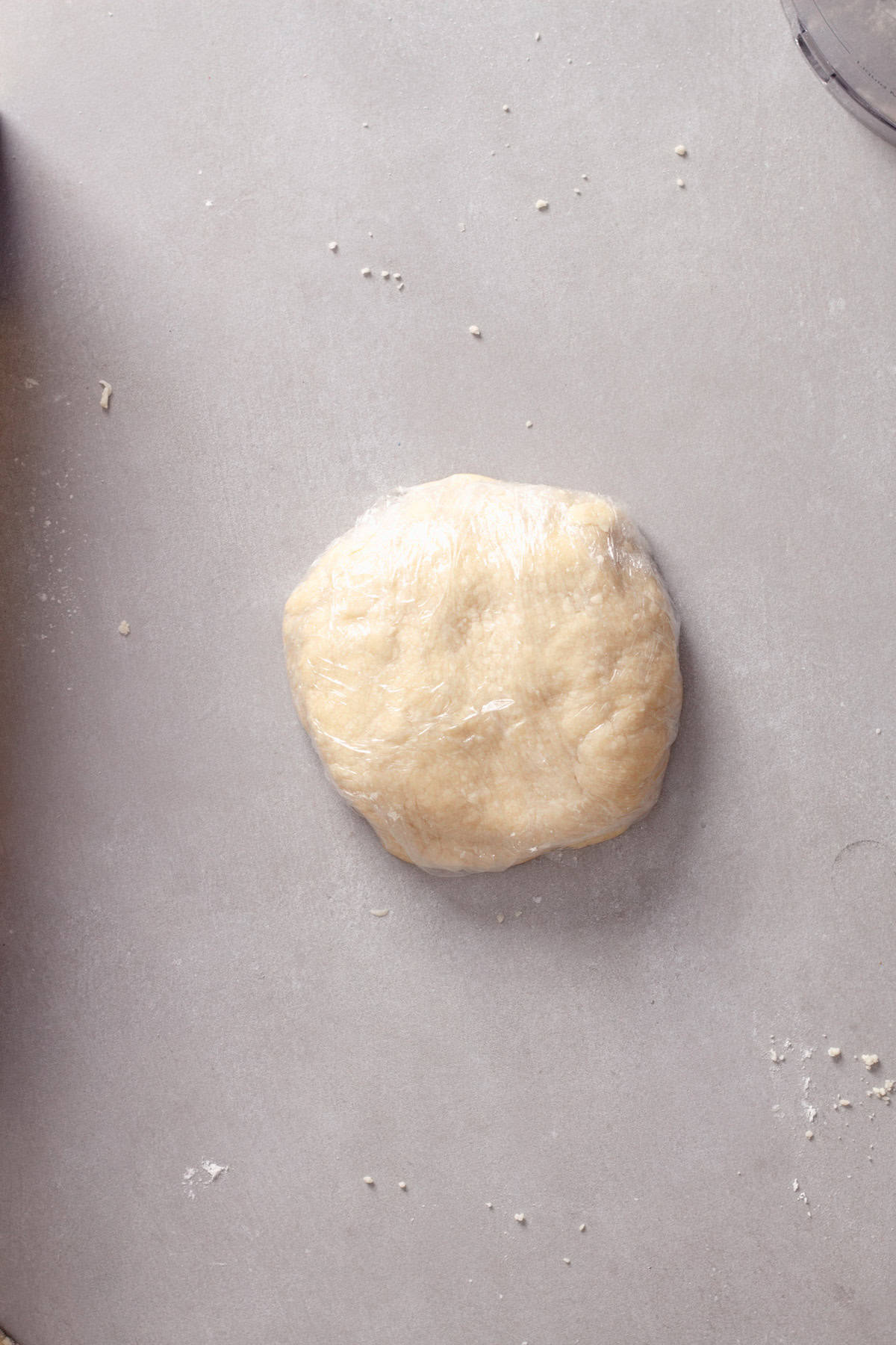 Homemade pie dough tightly wrapped in plastic wrap on a gray table.