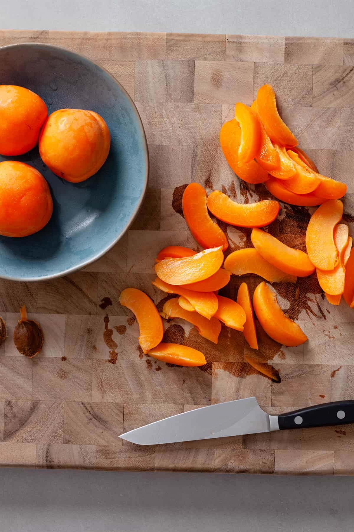 Apricots sliced on a butcher block cutting board.