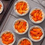 Several mini apricot tarts cooling on a wire rack on a gray table.