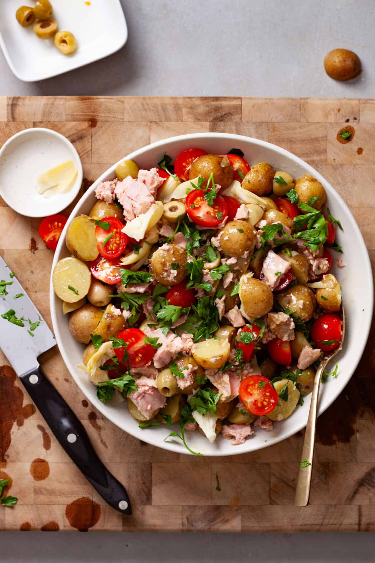 A mixing bowl of tuna and potato salad topped with fresh herbs on a cutting board.
