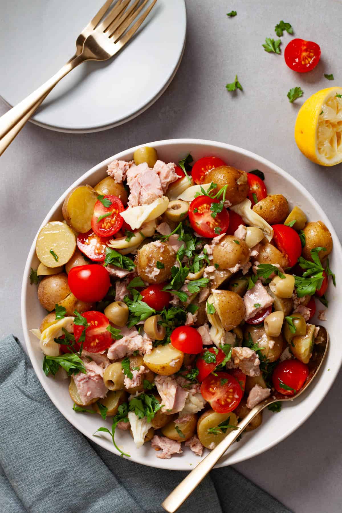 A mixing bowl of potato salad topped with tomatoes, herbs and tuna.