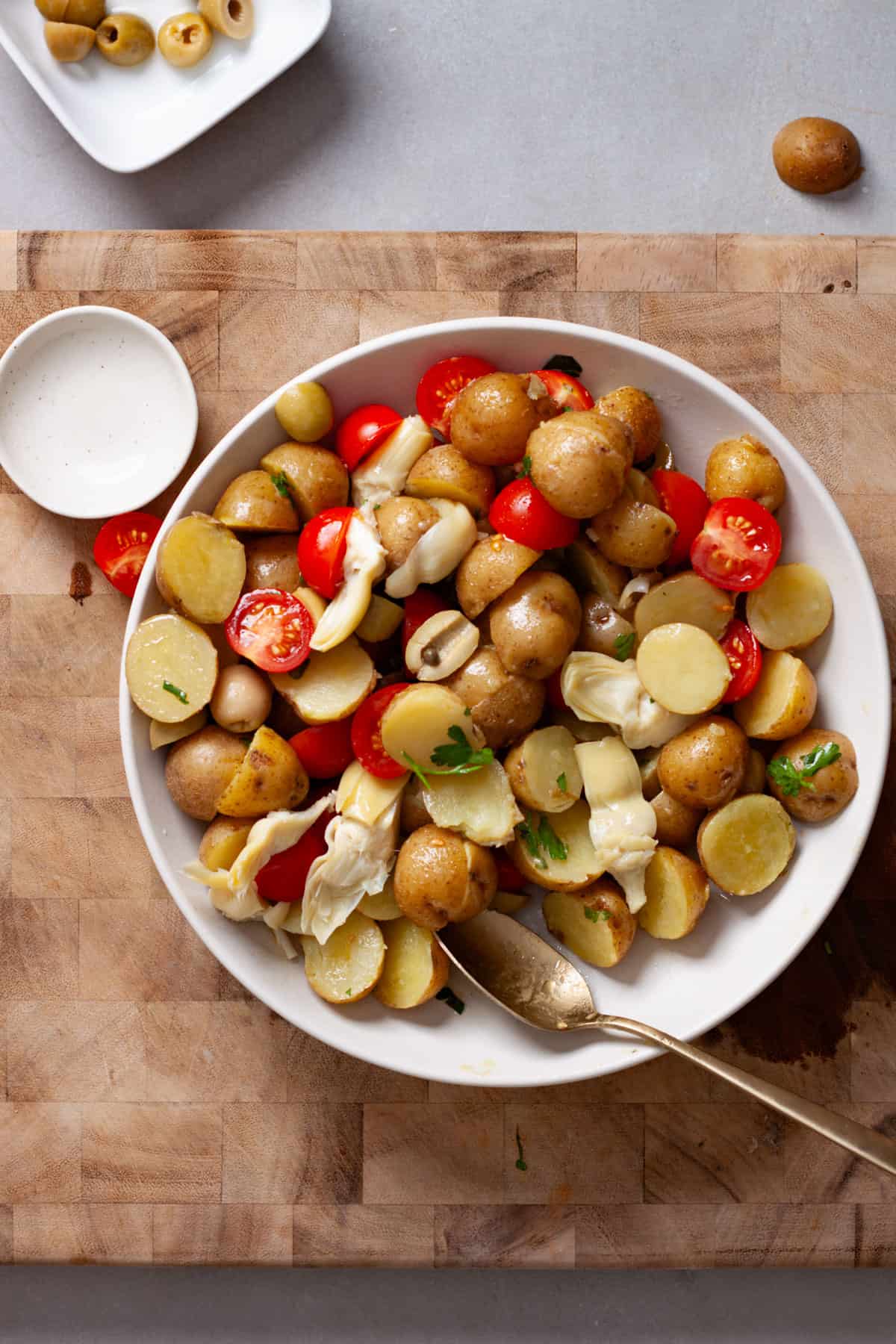 Potato salad with tomatoes and olives getting dressed with lemon vinaigrette.