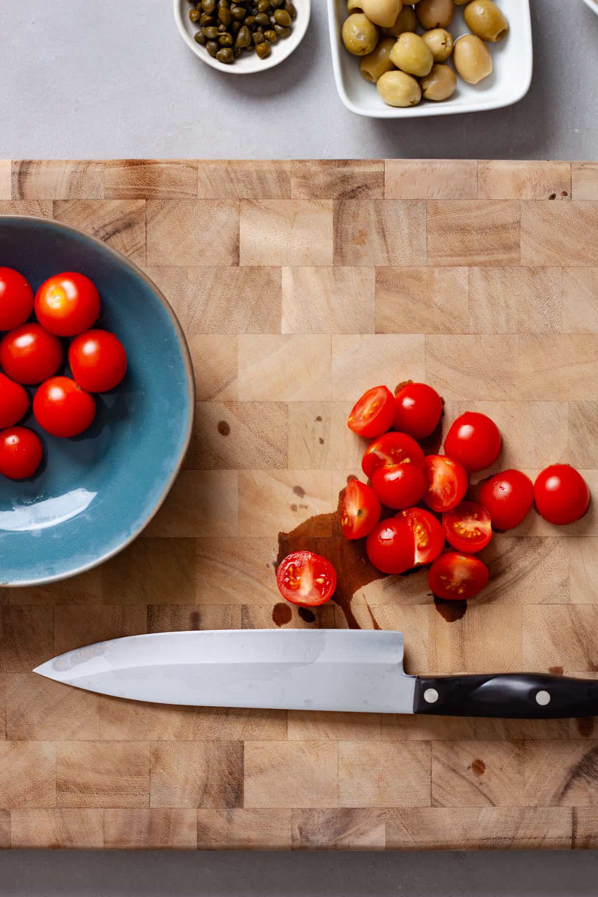 Cherry tomatoes getting chopped on a butcherblock cutting board.