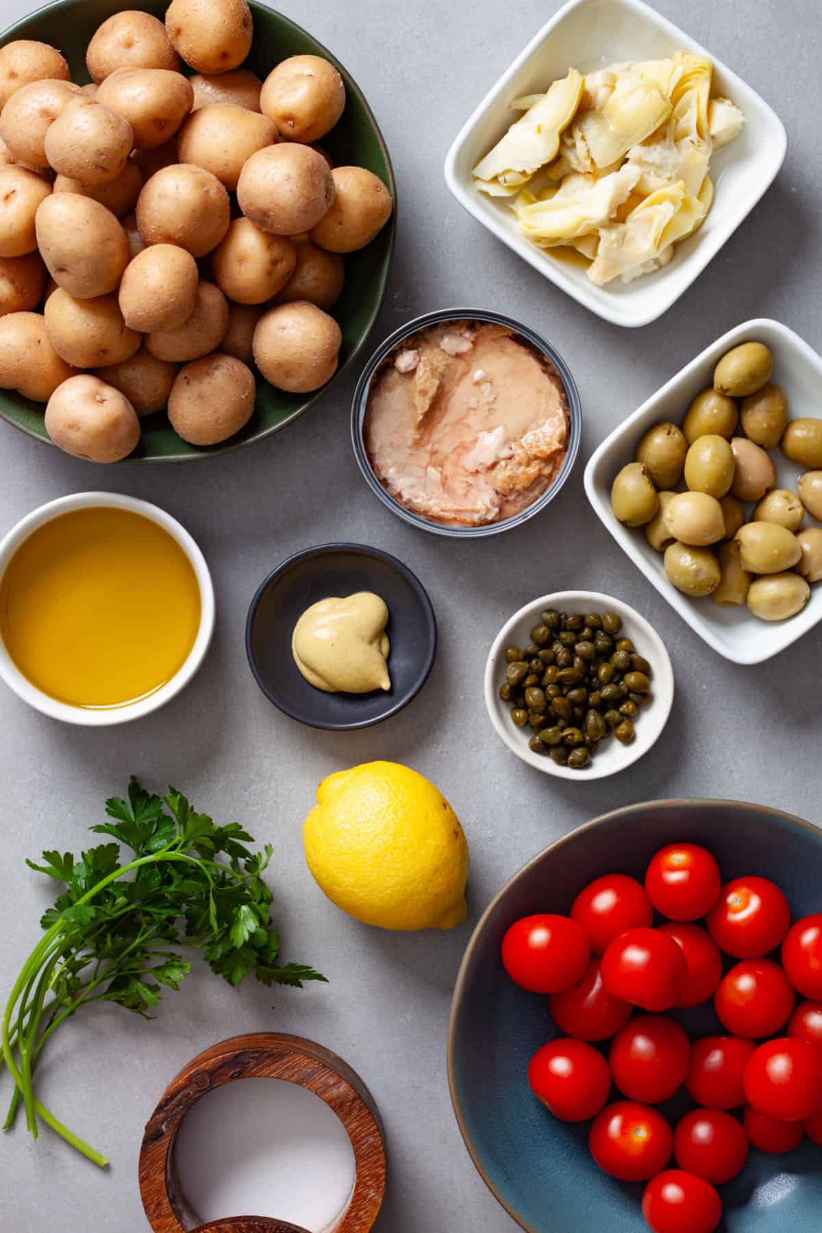 Ingredients for a potato salad with tuna and tomatoes on a gray table.