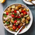 A big bowl of tuna potato salad on a napkin with two small plates of the salad off to the side.