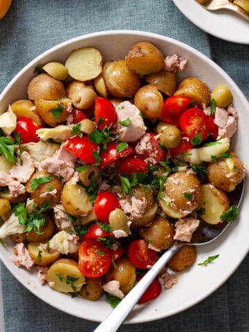 A big bowl of tuna potato salad on a napkin with two small plates of the salad off to the side.