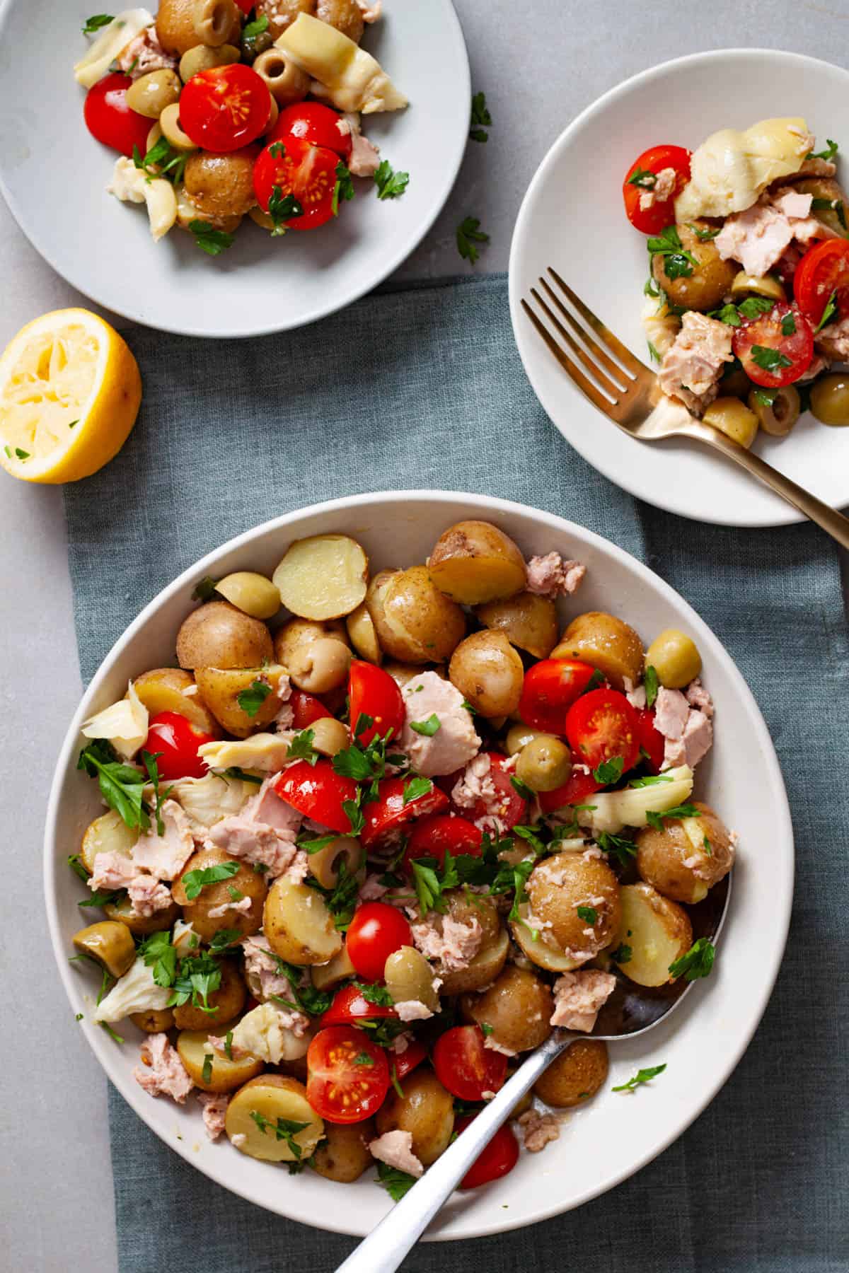 A big bowl of tuna potato salad on a napkin with two small plates of the salad off to the side.