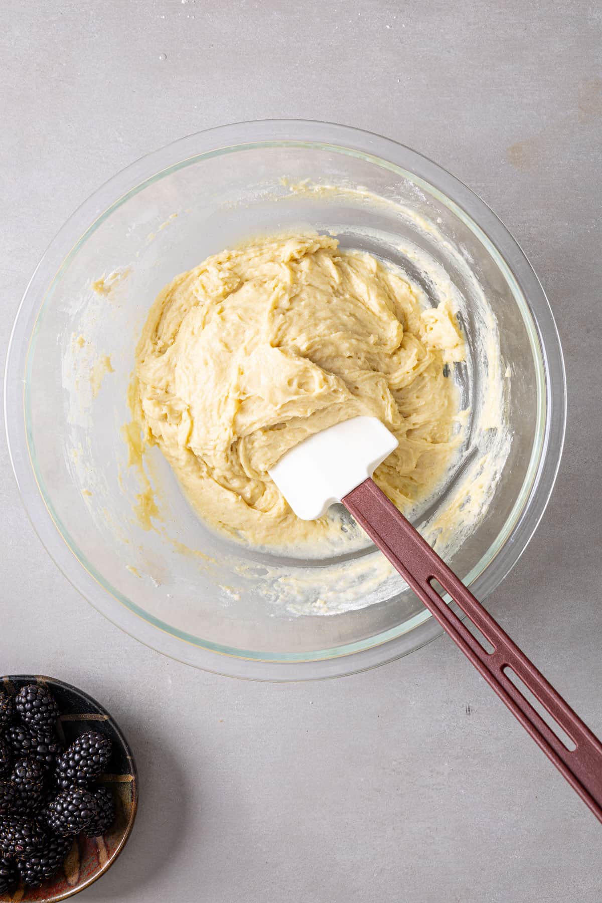A glass mixing bowl with a spatula stirring muffin batter.