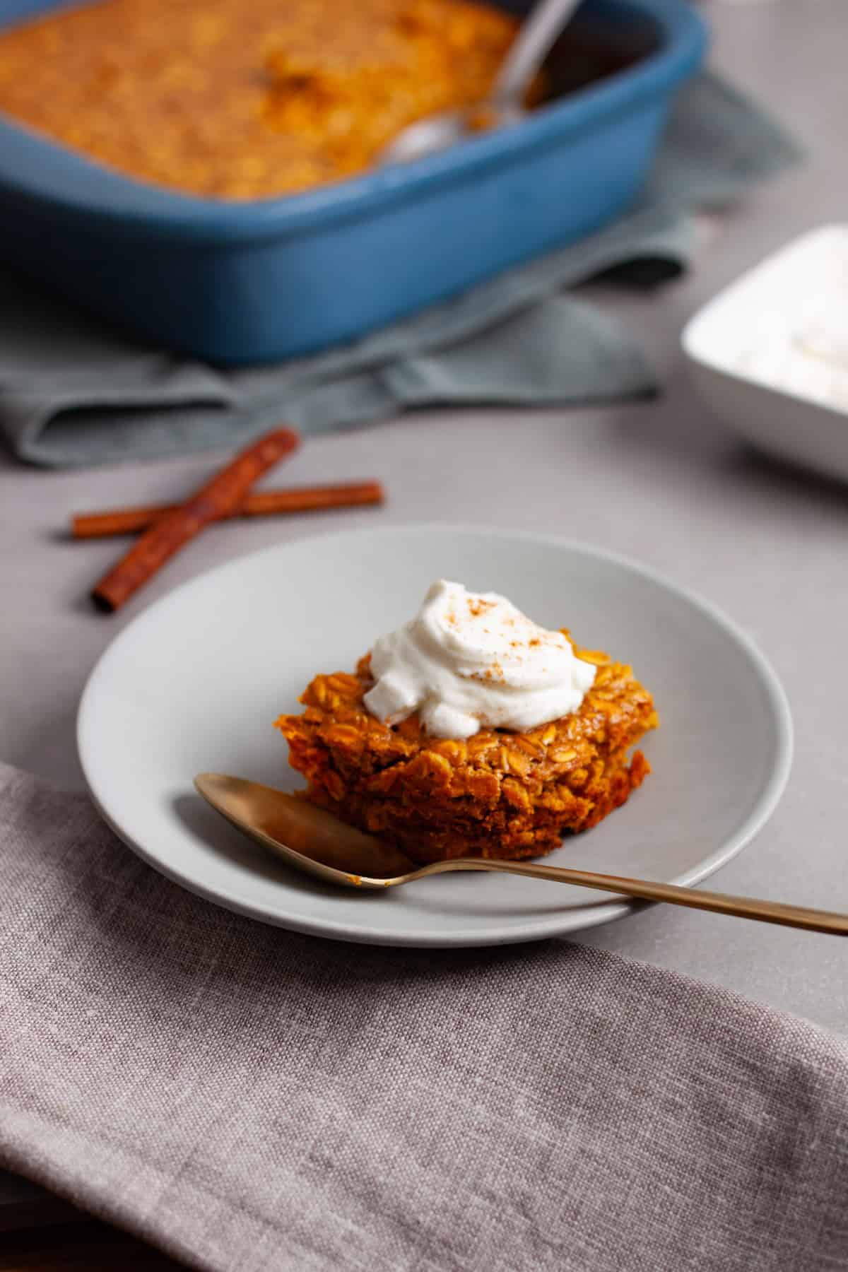 A serving of pumpkin pie baked oatmeal on a gray table topped with spiced yogurt.