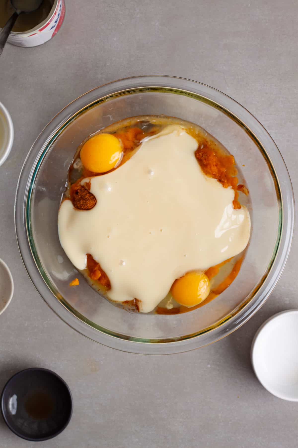 A glass mixing bowl with pumpkin puree, sweetened condensed milk and eggs for a baked oatmeal.