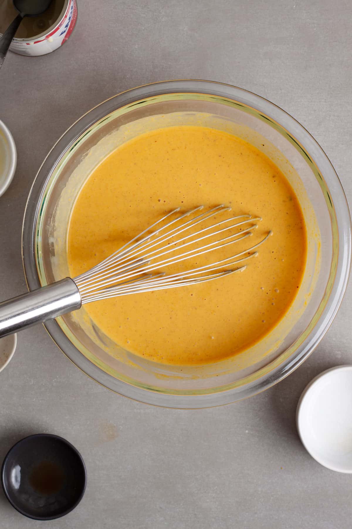 The wet ingredients for pumpkin pie baked oatmeal in a medium glass bowl on a gray table.