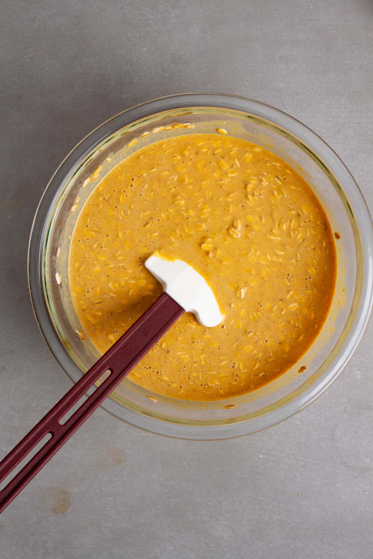 Uncooked pumpkin baked oatmeal in a medium glass bowl with a spatula stirring the mixture.