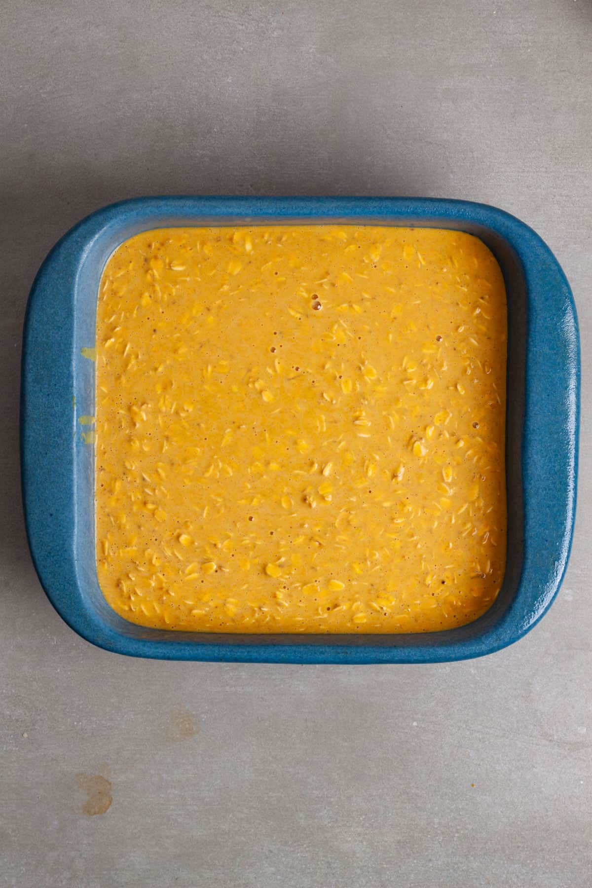 A blue square baking dish with uncooked pumpkin pie baked oatmeal on top of a gray table.