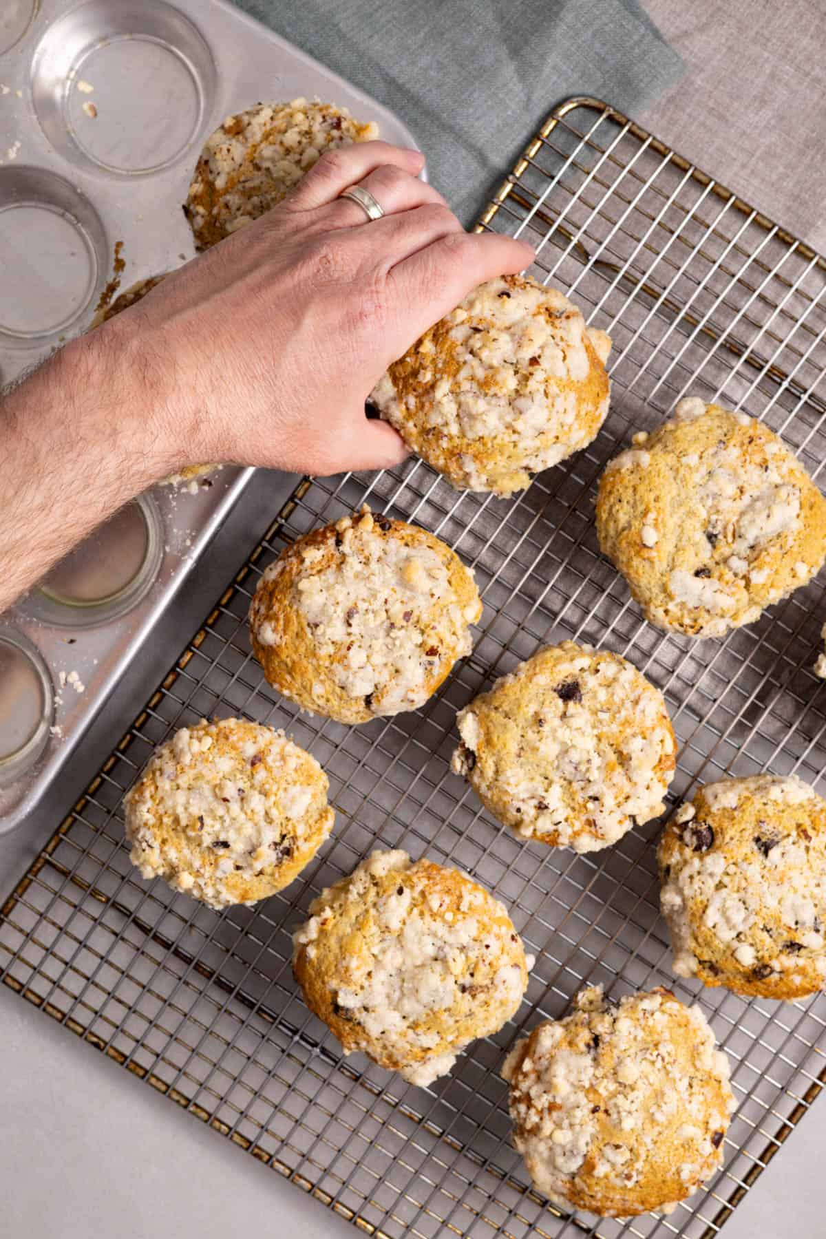 A hand moving Nutella stuffed muffins on a wire rack.