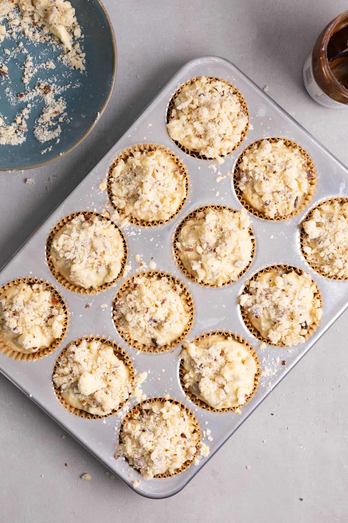 Streusel topping on a nutella stuffed muffins in a muffin tin.