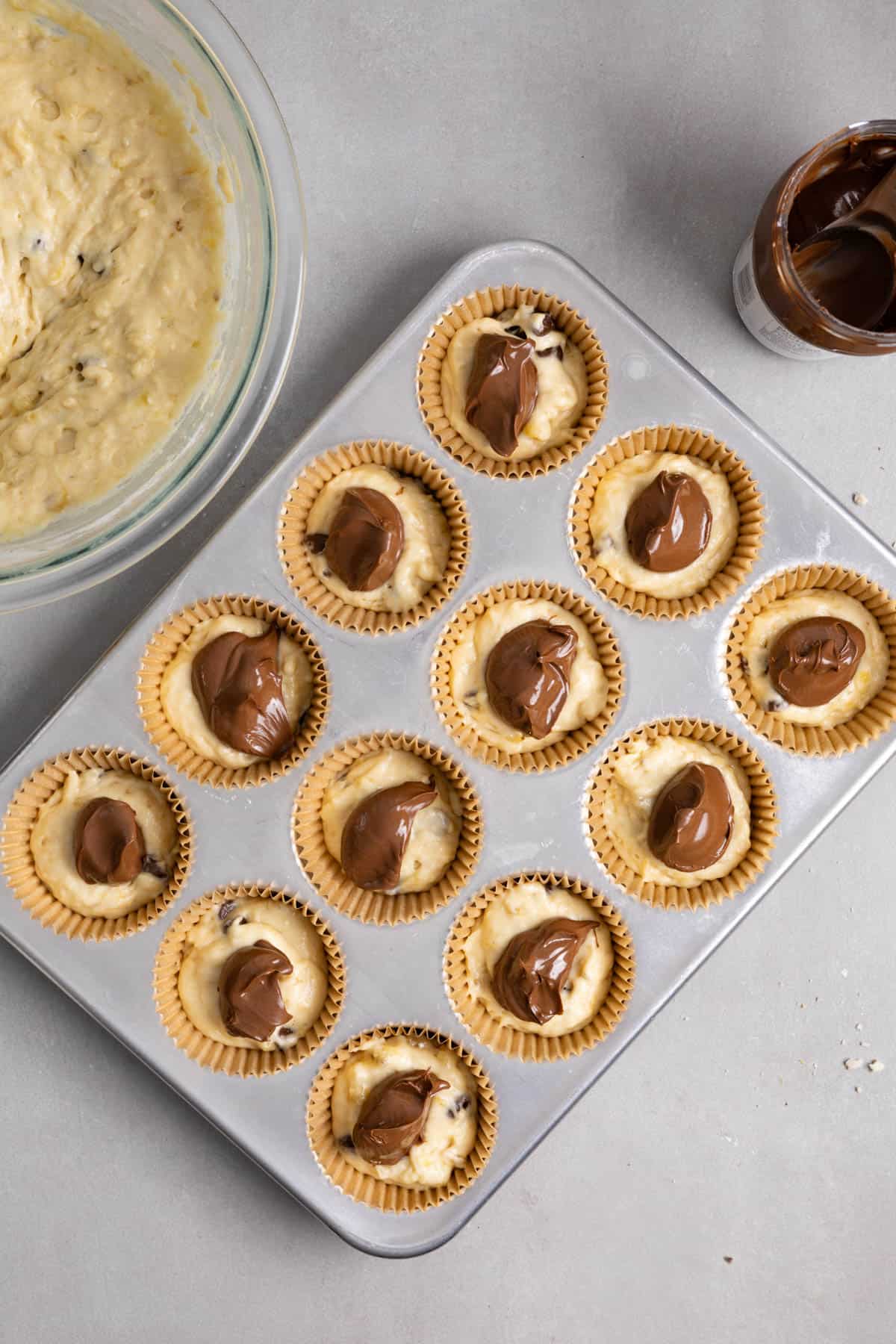 Nutella spooned onto muffin batter in a muffin tin.