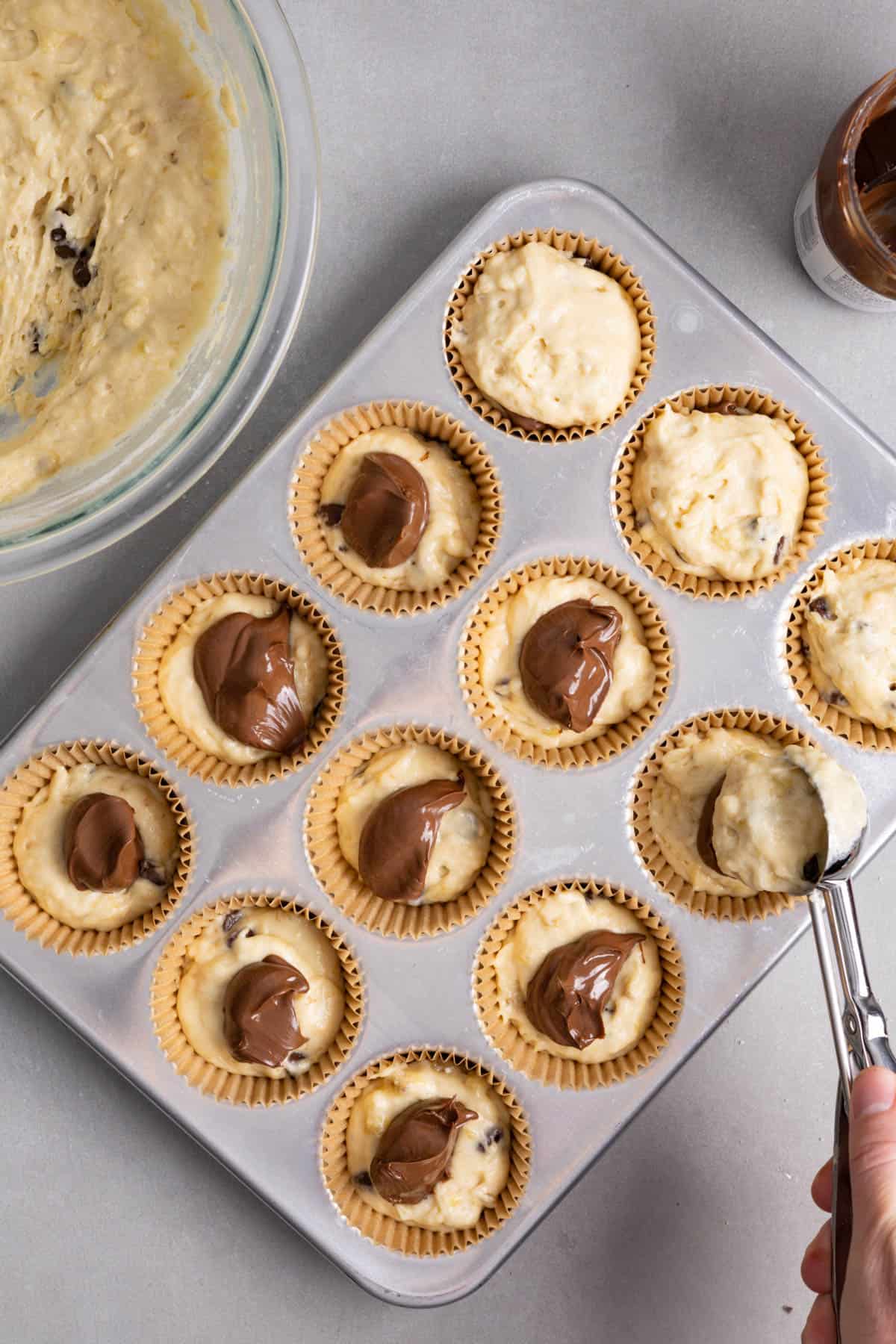Muffin batter getting scooped on top of nutella filled muffin cups.