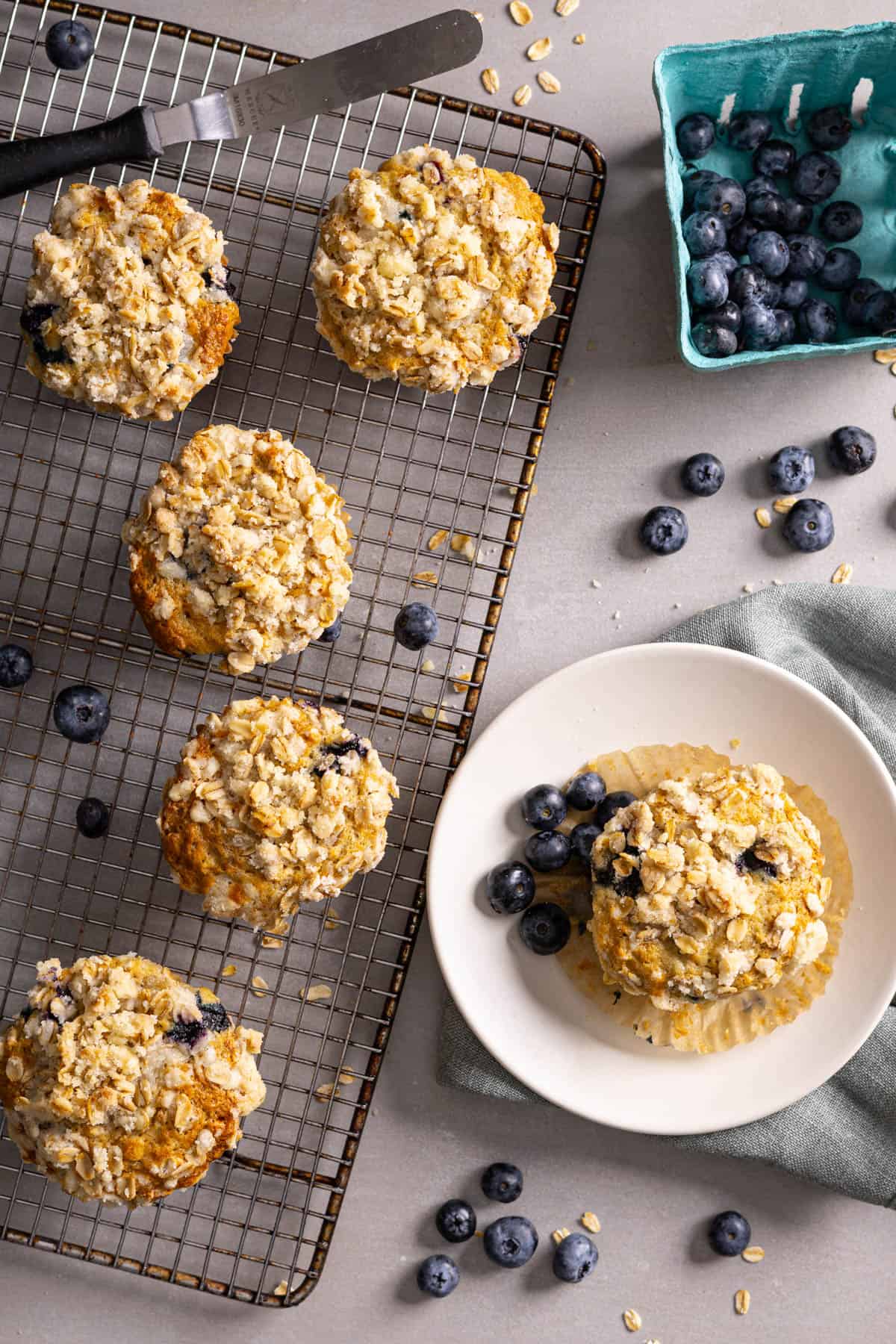 Blueberry banana oat muffins cooling on a rack and a plate with a single muffin.