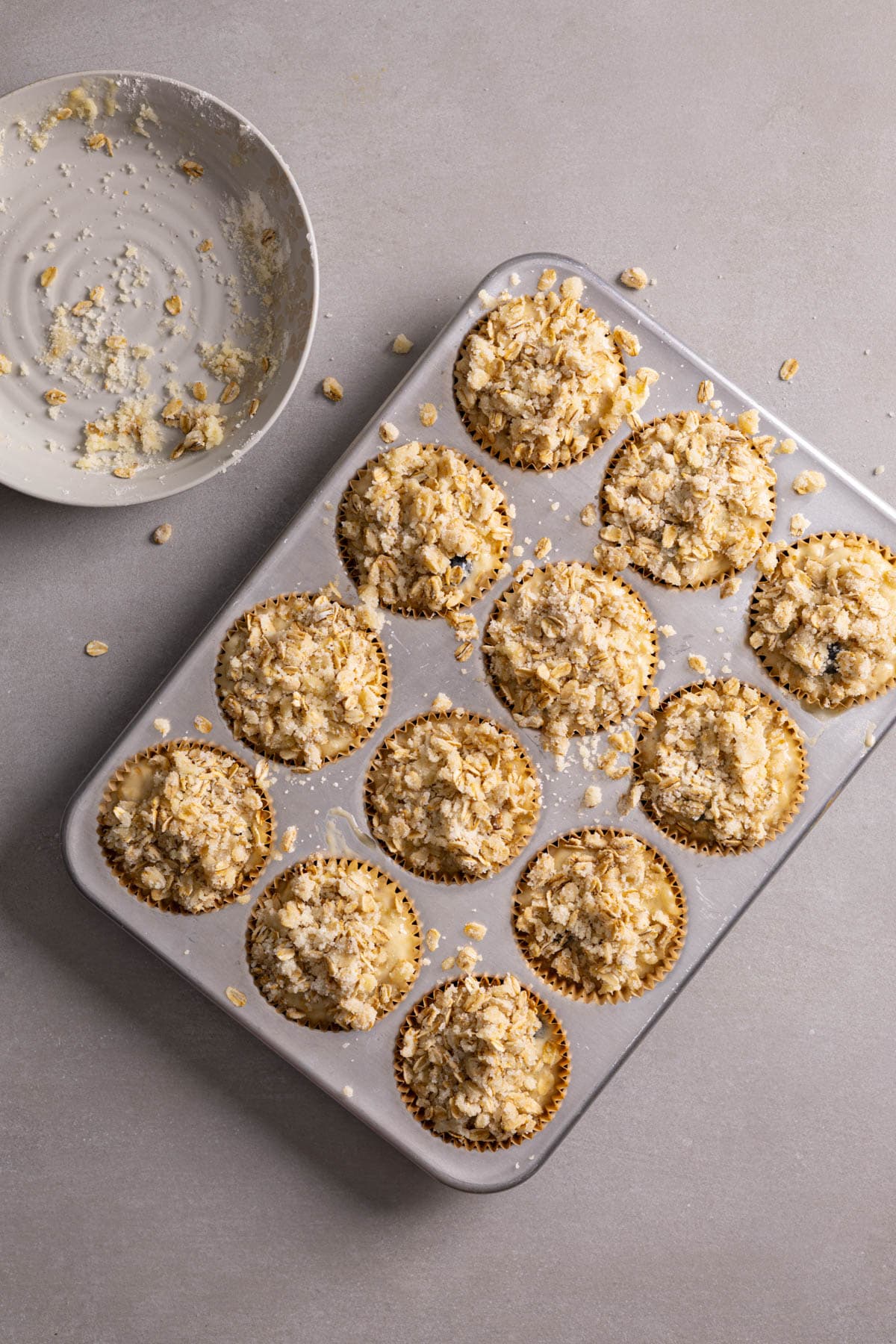 Streusel topping added to the top of muffins in a muffin tin.