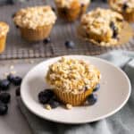 Blueberry banana oat muffins on a wire rack with a single serving on a plate.