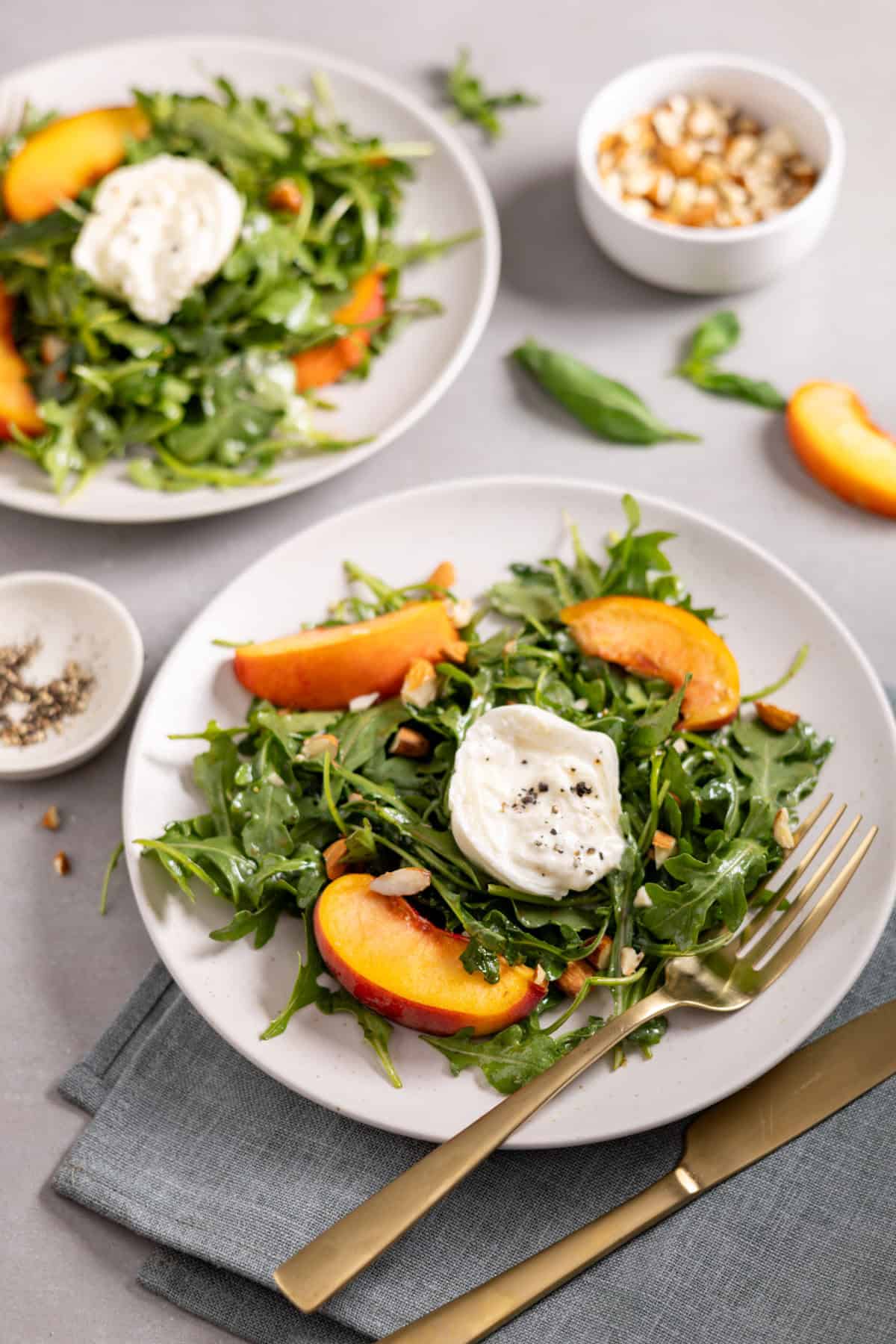 Two plates of arugula burrata salad topped with peaches and almonds.