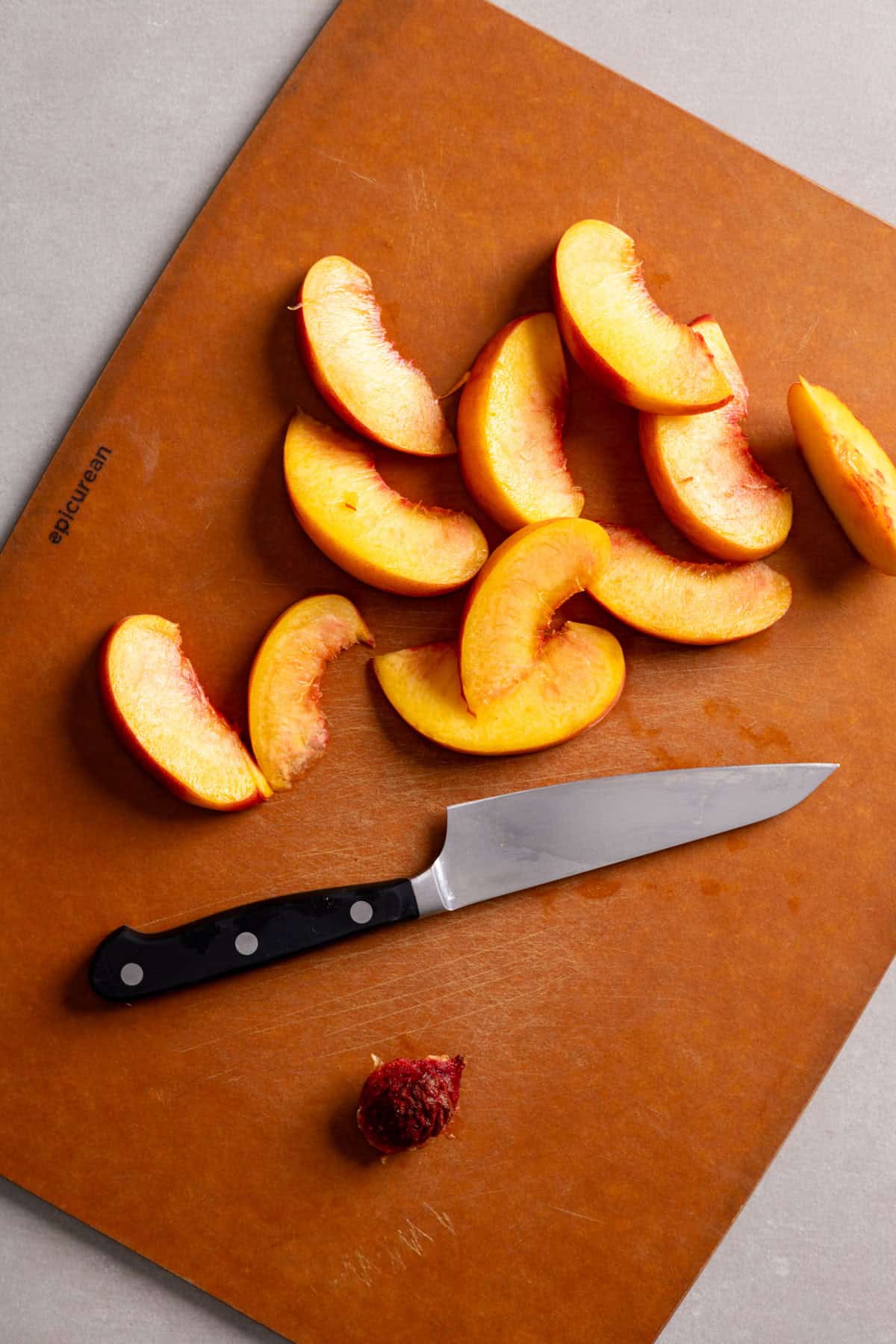 Peaches sliced with a small knife on a cutting board.